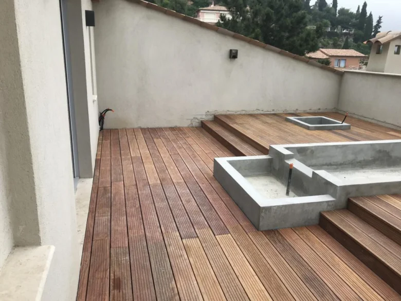 Vyvysená dřevěná terasa s betonovými květináči a schodišti.