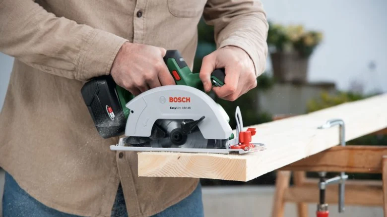 Muž řezá dřevo bezdrátovou kruhovou pilou značky Bosch.
