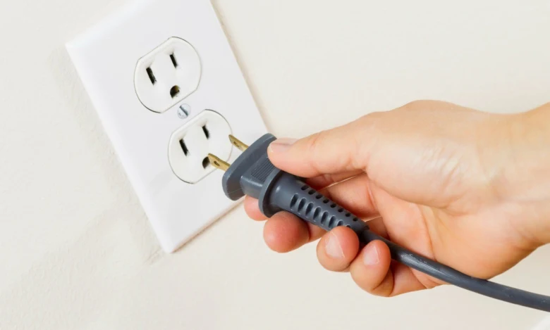 Ruka zapojuje šňůru do elektrické zásuvky na zdi.