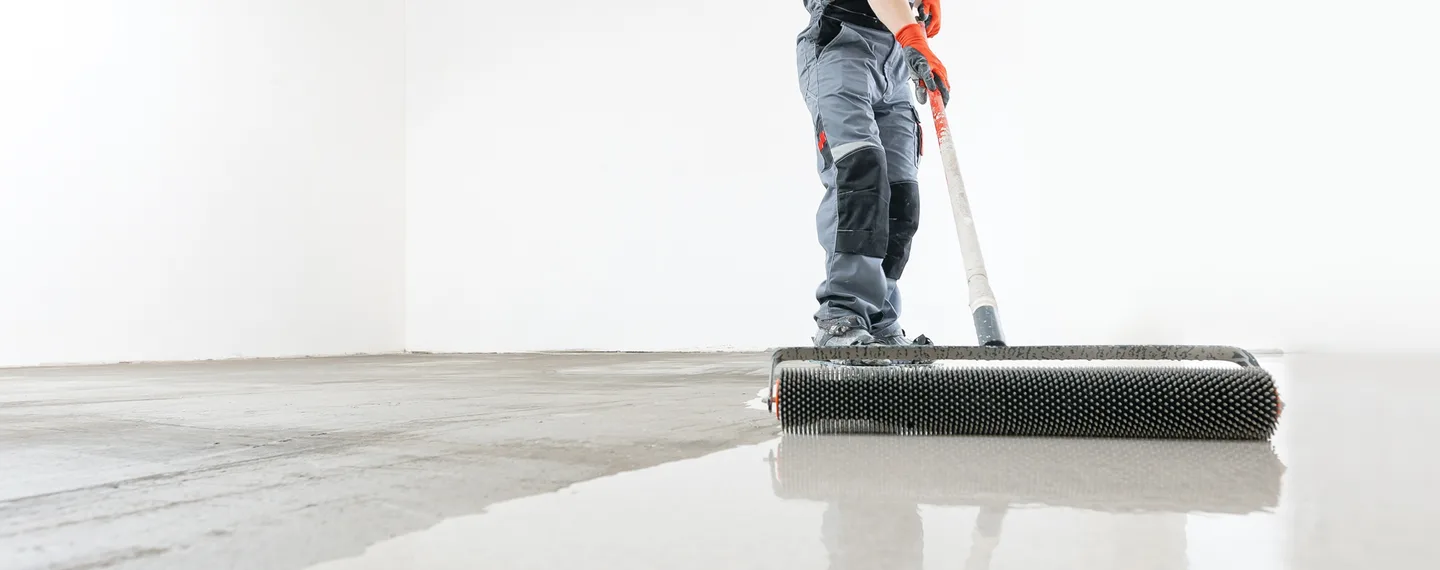 Pracovník aplikuje kartáčovaný beton na podlahu pomocí válcování.
