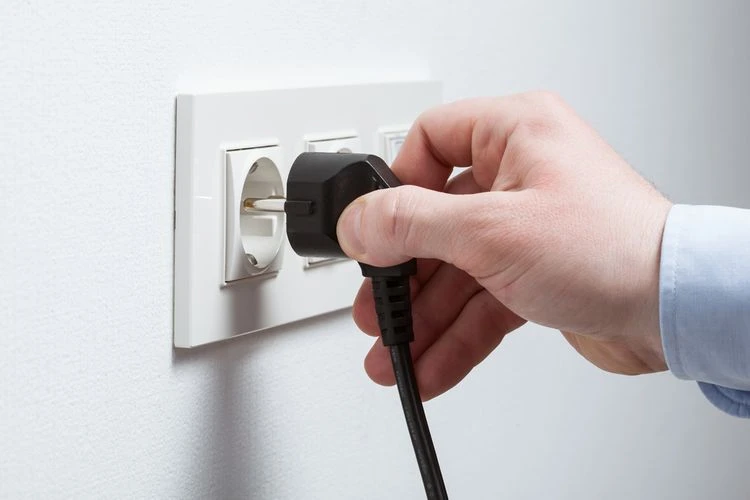 Ruka zapojuje černý elektrický zástrčku do bílé zásuvky na zdi.