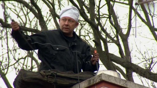 Muž opravuje komín na střeše s nástroji v rukou.