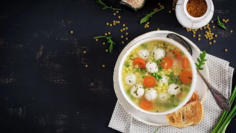 Hot chicken soup served in white bowl with bread.