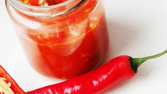 Sklenice s chilli omáčkou vedle čerstvých papriček