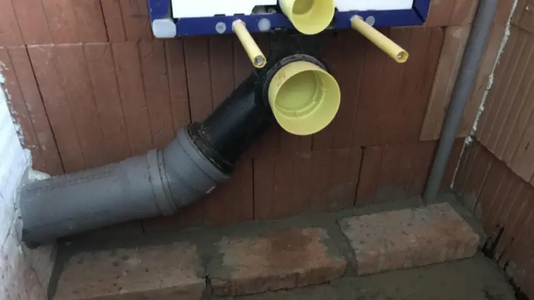 Instalace geberitu s viditelnými potrubími a žlutými přípojkami.