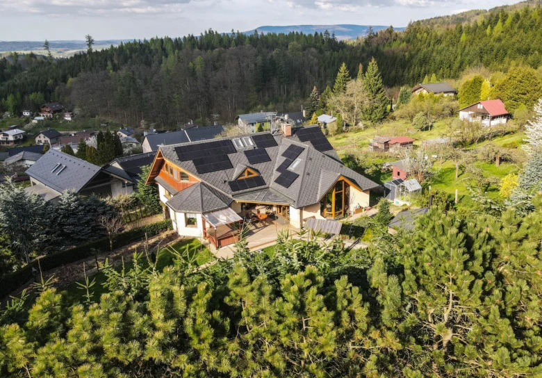 Dům s fotovoltaickými panely na střeji v přírodě.