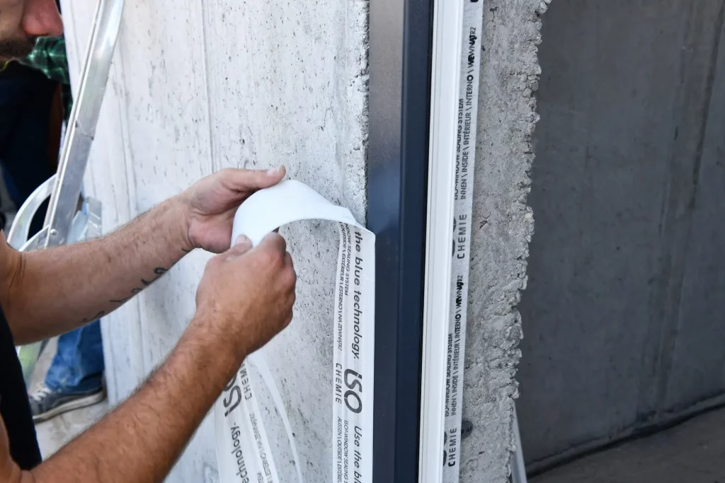 Instalace rámu okna s aplikací izolační pásky na betonovou stěnu.