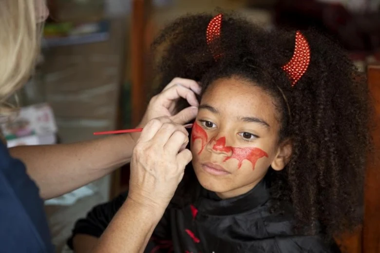 Dívka se maluje na čerta pro Halloween doma.