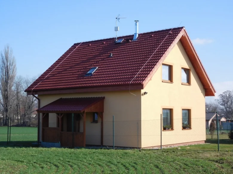 Moderní dřevostavba s červenou střechou na zelené louce.
