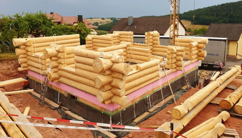 Stavba dřevostavby z kmenů na základové desce v Praze.