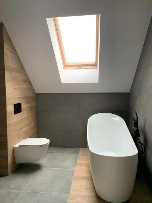 Moderní koupelna s vanou a WC pod střešním oknem.