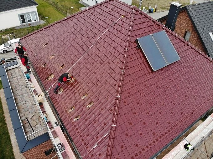 Dva dělníci montují fotovoltaické panely na červenou střechu.