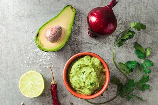 Avokádo s ingrediencemi pro guacamole na šedém pozadí.