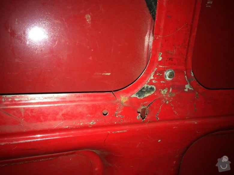 Poškozený červený panel dveře automobilu s odškrábanou barvou.