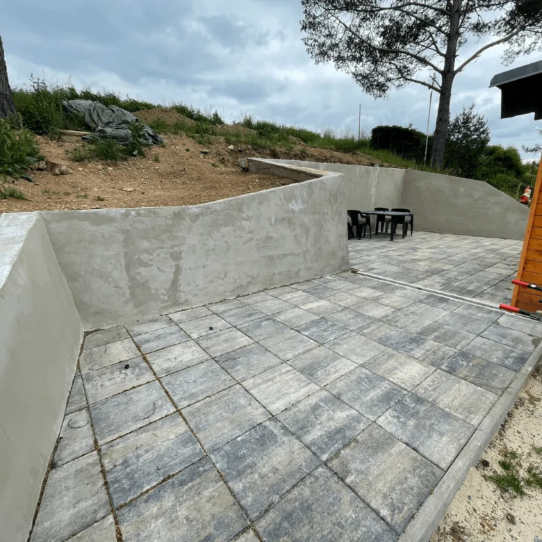 Hotová vyvýšená terasa s kamennou dlažbou a betonovými zídkami.