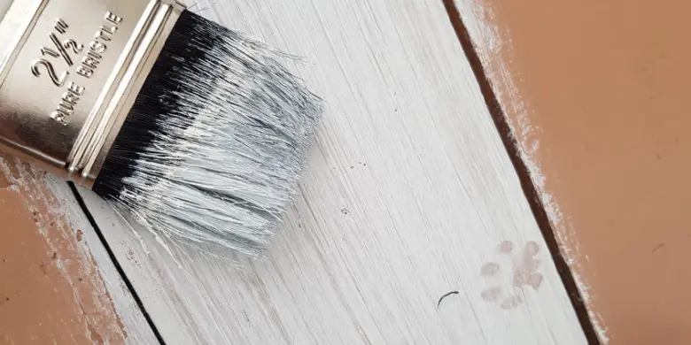 Křídový štětec nanáší bílou barvu na dřevo.