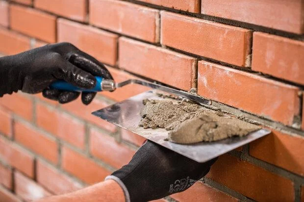 Stavebník nanáší maltu na cihly pomocí malého špachtle.