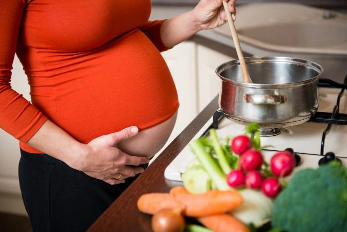 Těhotná žena vaří zdravé jídlo s čerstvými zeleninovými surovinami.