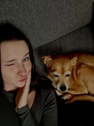 Žena leží na gauči vedle svého hnědého psa.