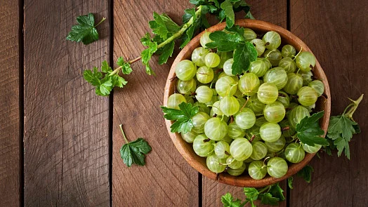 Čerstvé angrešty v dřevěné misce na tmavém dřevěném povrchu.