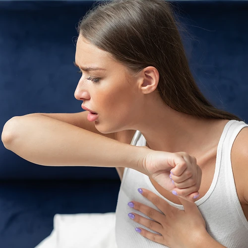 Žena kašle do lokte, ukazuje správnou hygienu při kašlání