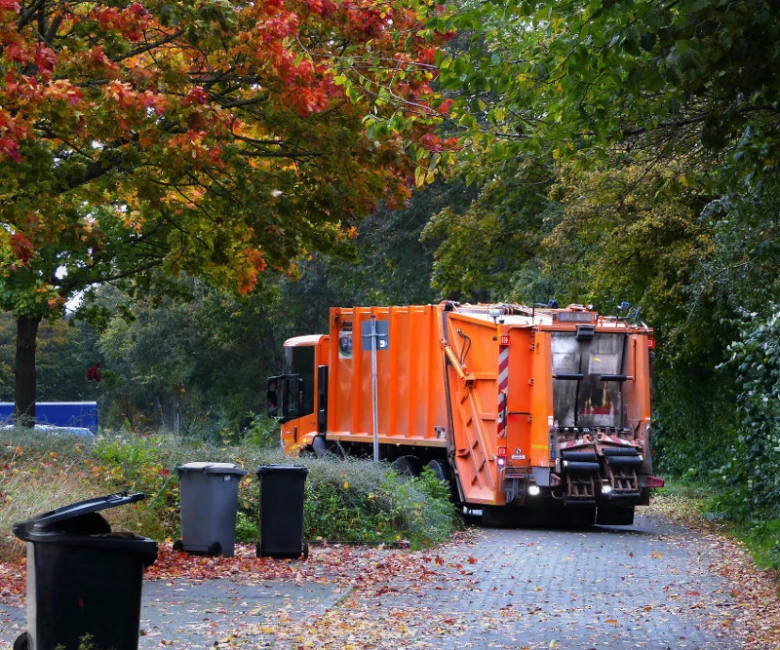 Oranžový sběrný vůz popelnice na ulici s koši.