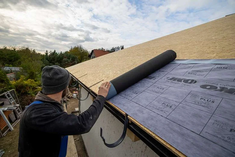 Muž položí hydroizolační fólii na střešní konstrukci.