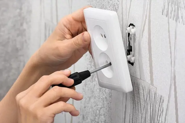 Ruce montují elektrickou zásuvku do stěny šroubovákem.