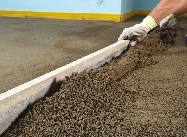 Pracovník vyrovnává vlhký kartáčovaný beton pomocí dřevěného úhlového nástroje.
