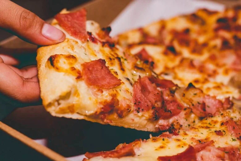 Ruka zvedá kousek pizzy s toustovou hranou.
