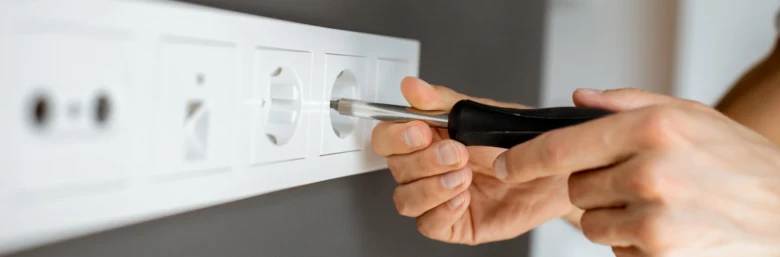 Osoba montuje elektrickou zásuvku šroubovákem do zdi.