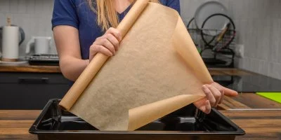 Člověk rozkládá pečicí papír na plech v kuchyni.