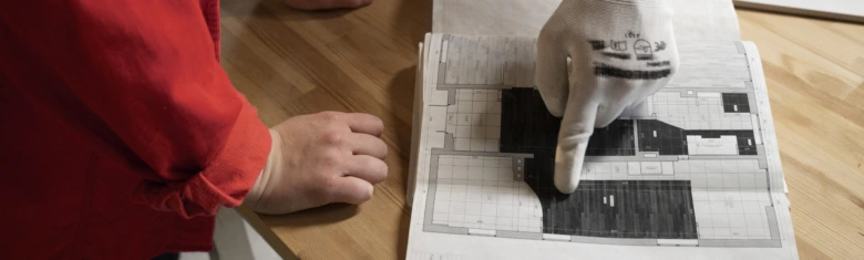 Ruce ukazují na plán rekonstrukce garsonky s označenými místy.