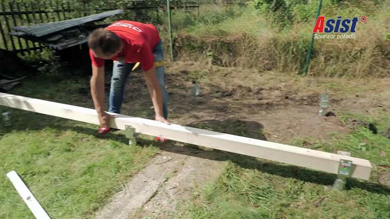 Muž sestavuje dřevěný rám venku na trávníku.
