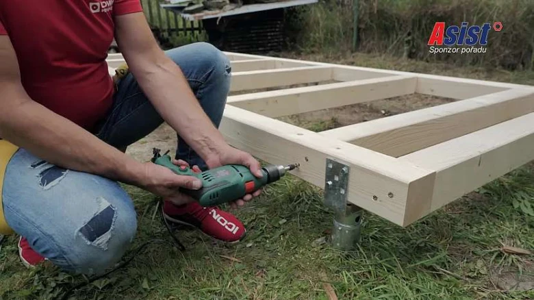 Muž sestavuje dřevěný rám pomocí elektrického vrtáku venku.
