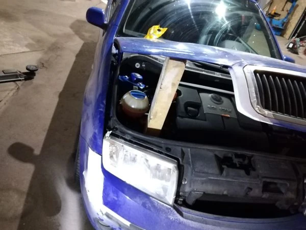 Modrý Škoda s otevřenou motorkou v dílně na opravu karoserie.