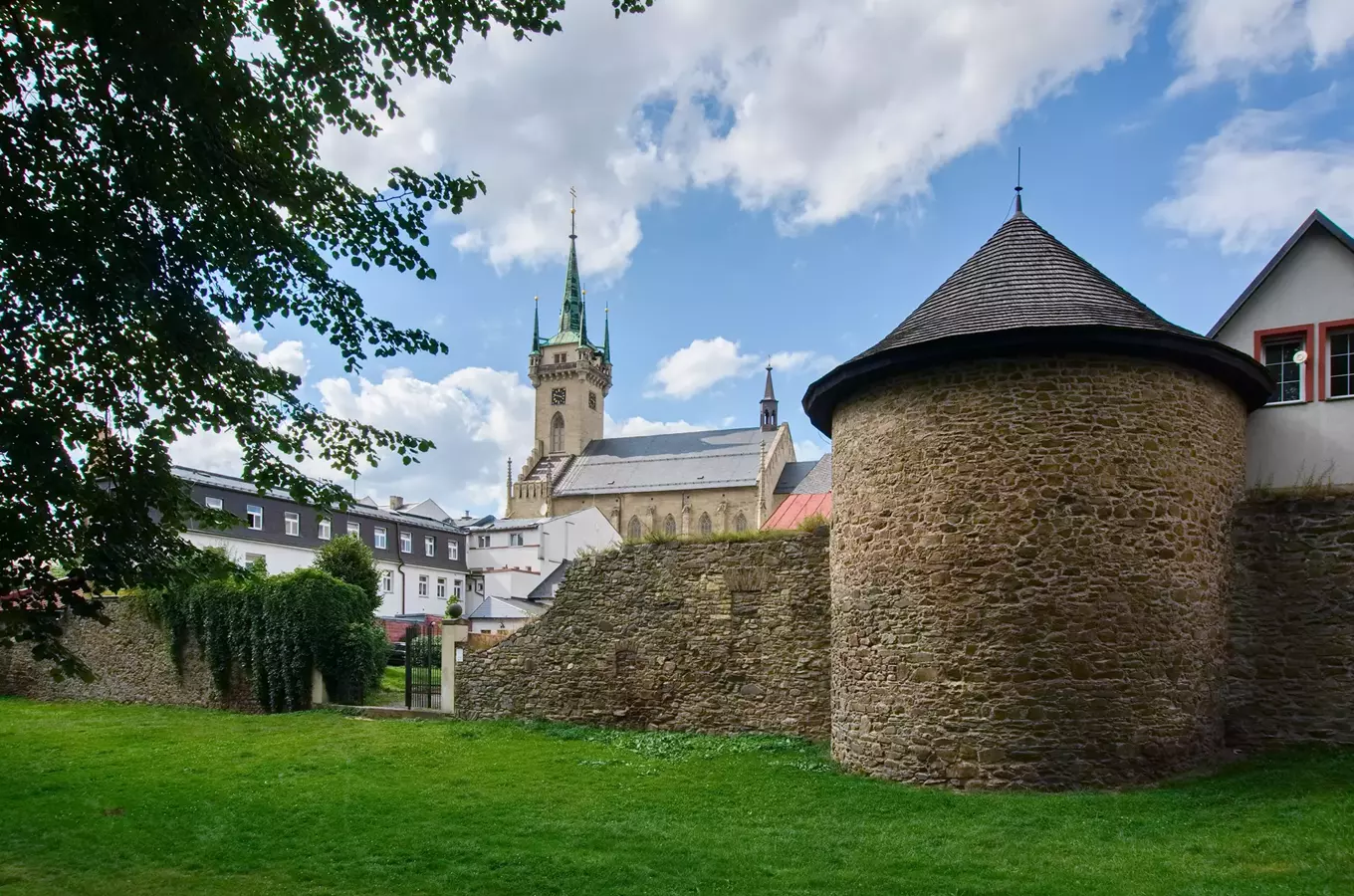Historická kamenná věž s kostelem na pozadí v českém královském městě.