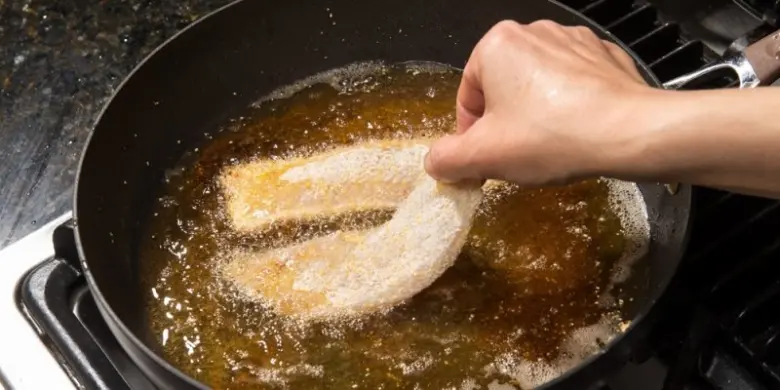 Ruce kladou obalený ryba do horkého oleje.