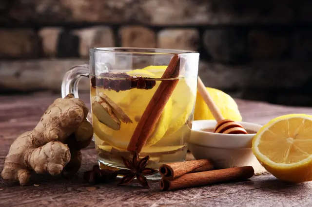 Sklenička s horkým nápojem z ingveru a citronu se skořicí.
