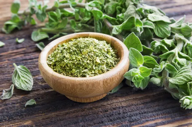 Sušené čerstvé oregano v dřevěné misce na tmavém stole.