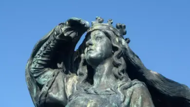 Bronzová socha korunované ženy s dlouhými vlasy na modré obloze.