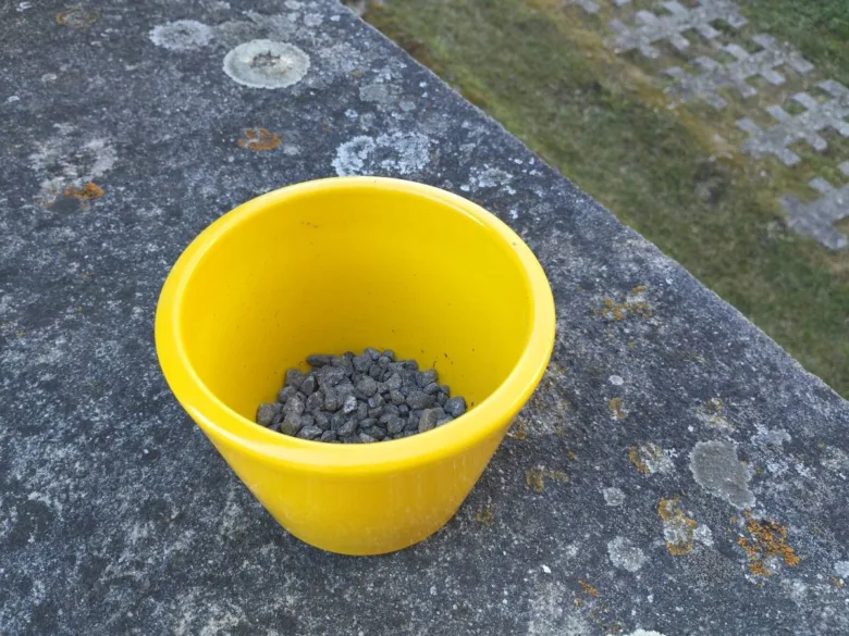 Žlutý hrnec s keramzitem na kamenné ploše venku.
