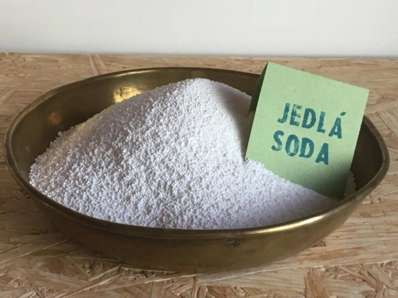 Hromada jedlé sody v kovové misce vedle zelené karty.