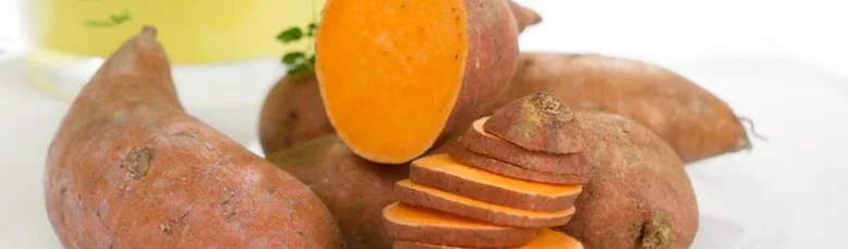 Batáty s řezaným kouskem ukazující oranžovou dužinu.