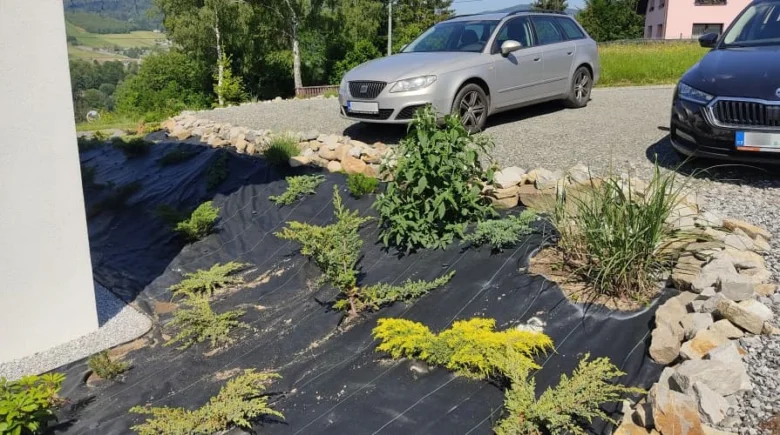 Černá geotextilie s rostlinami na svahu zahradního pozemku