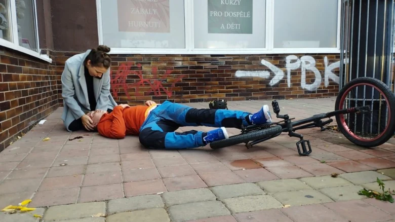 Žena poskytuje první pomoc zraněnému dítěti po pádu s bicyklem.