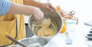 Osoba míchá těsto v misce na kuchyňském stole.
