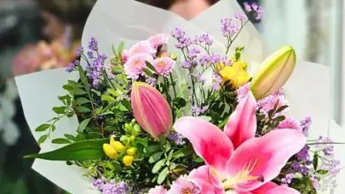 Květinová vazba s liliiemi a fialovými květy v bílém papíru.