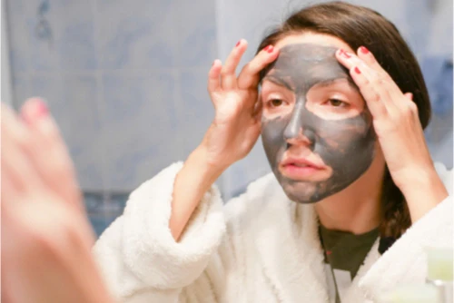 Žena nanáší tmavou tvářovou masku s uhlím na obličej.