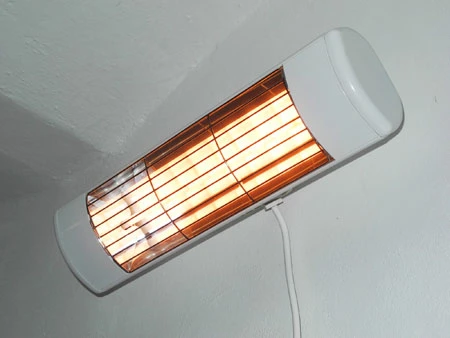 Bílý elektrický infra topný panel na stěně s viditelnými žhavícími prvky.